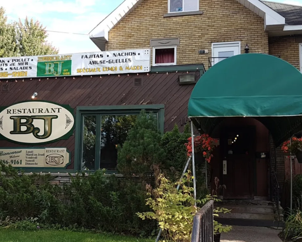 Façade du restaurant avec l'enseigne "Restaurant BJ, EST 1988", la bannière des spécialités et l'auvent vert