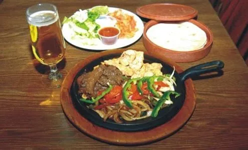 Assiette de fajitas sur poêlon en fonte, servie avec salade, riz et tortillas, avec une bière